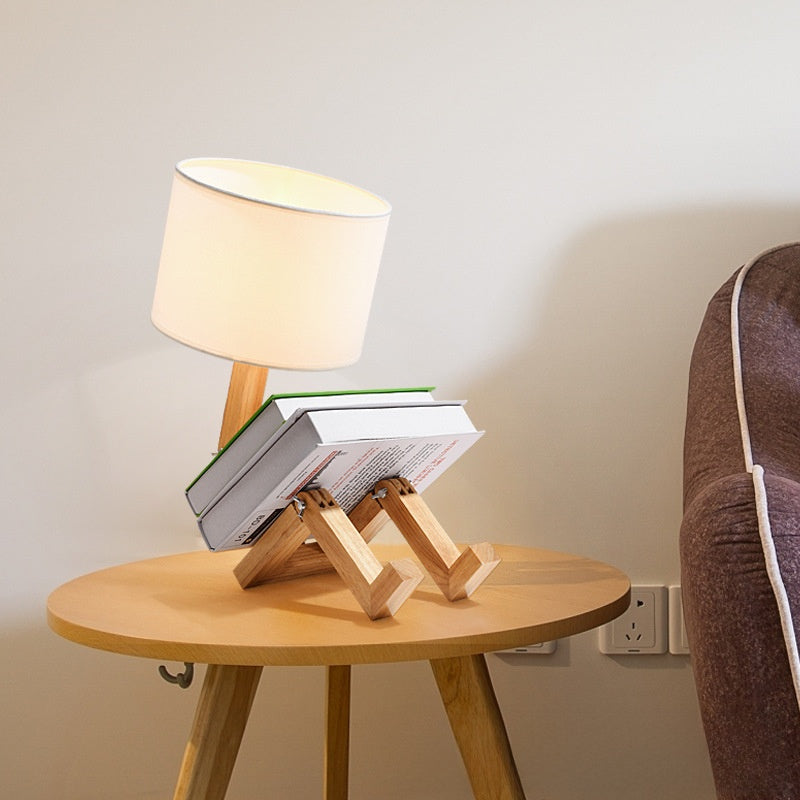 Robot Lamp — a jointed wooden figure sitting with its legs out, holding a fabric lampshade overhead