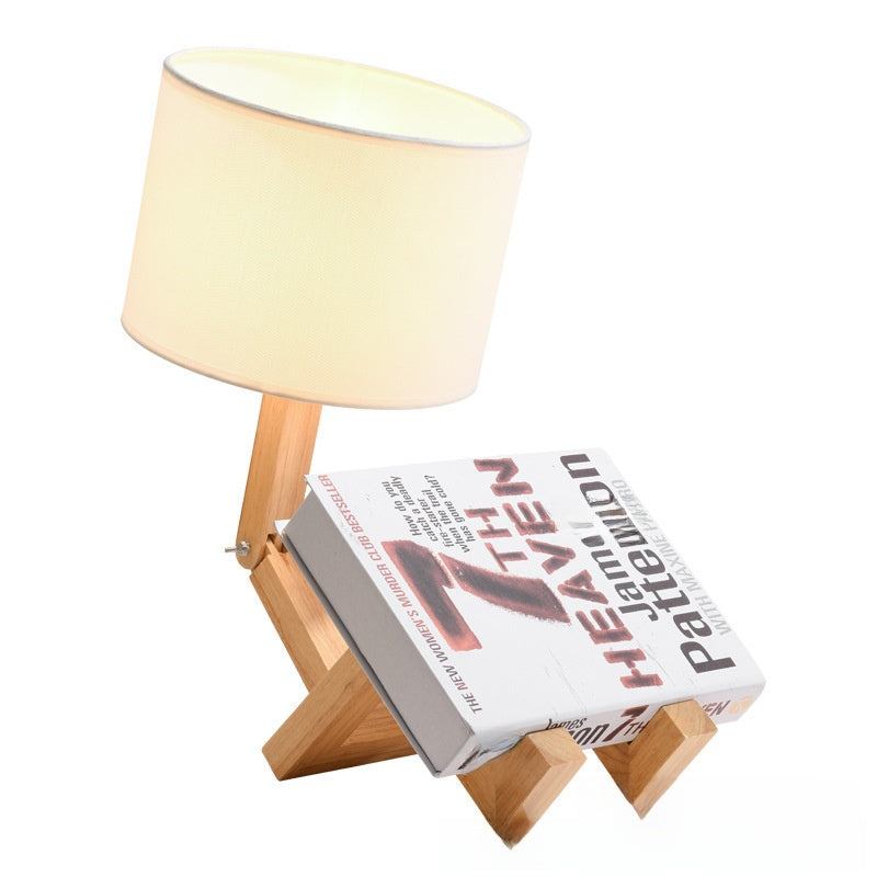 Robot Lamp — a jointed wooden figure sitting with its legs out, holding a fabric lampshade overhead