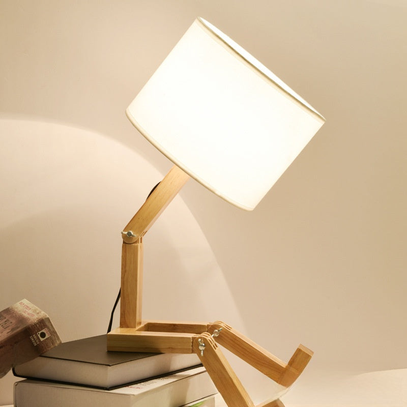 Robot Lamp — a jointed wooden figure sitting with its legs out, holding a fabric lampshade overhead