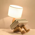 Robot Lamp — a jointed wooden figure sitting with its legs out, holding a fabric lampshade overhead